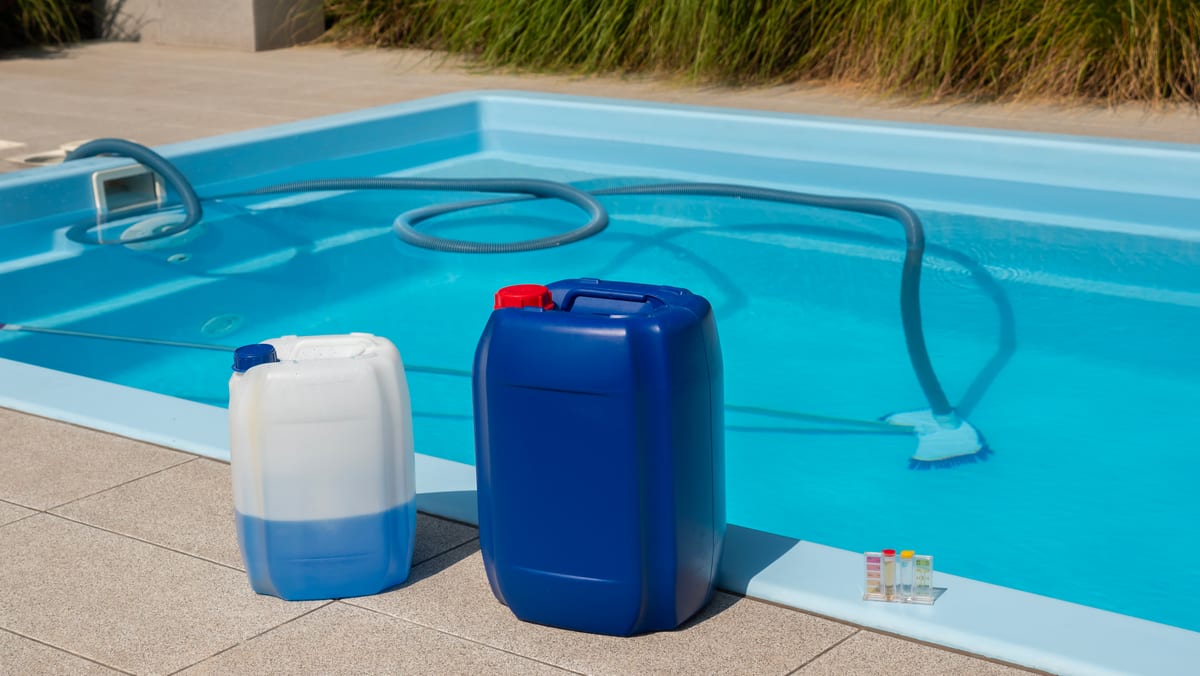 Pool vacuum hose in the water with chemical canisters staged at the edge of a residential pool
