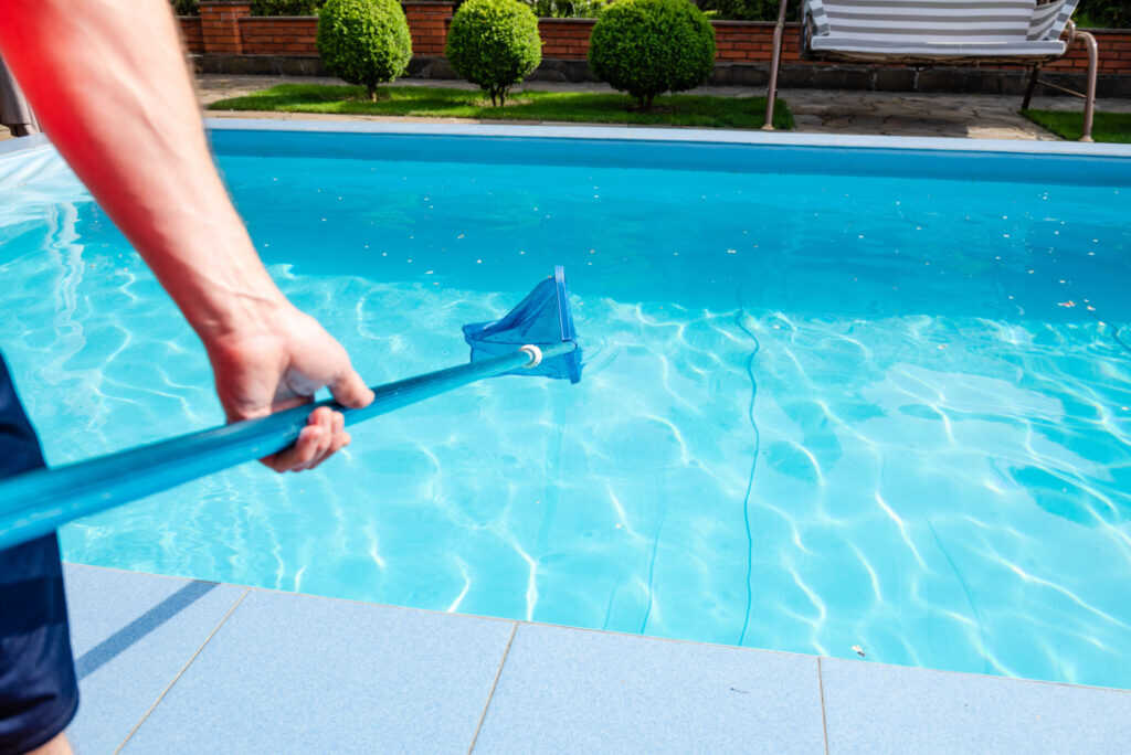 Pool service technician skimming a residential swimming pool