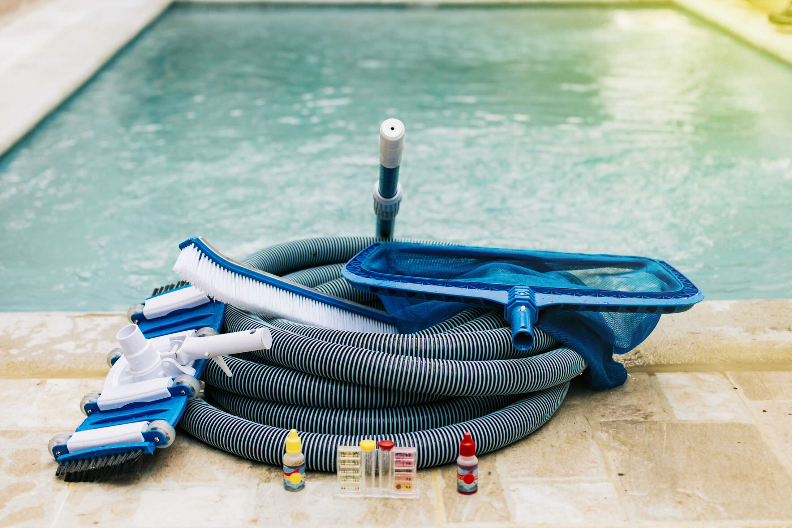 Pool cleaning maintenance tools including vacuum, pH test kit, and leaf skimmer